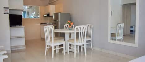 Una cocina compacta con refrigerador, estufa y microondas. Hay una mesa de comedor con cuatro sillas y un florero con flores. Un espejo grande está en la pared.