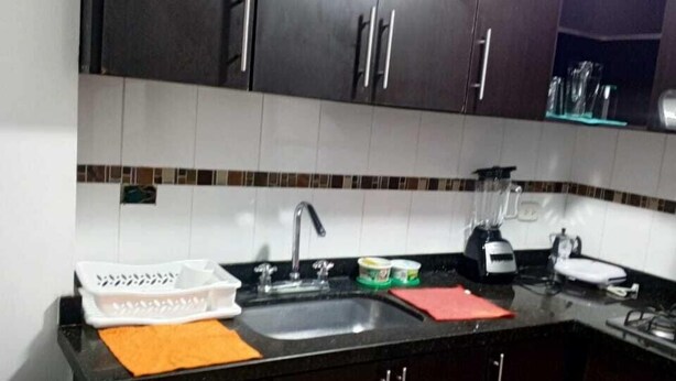 Una cocina con armarios oscuros, encimera negra y un lavamanos.