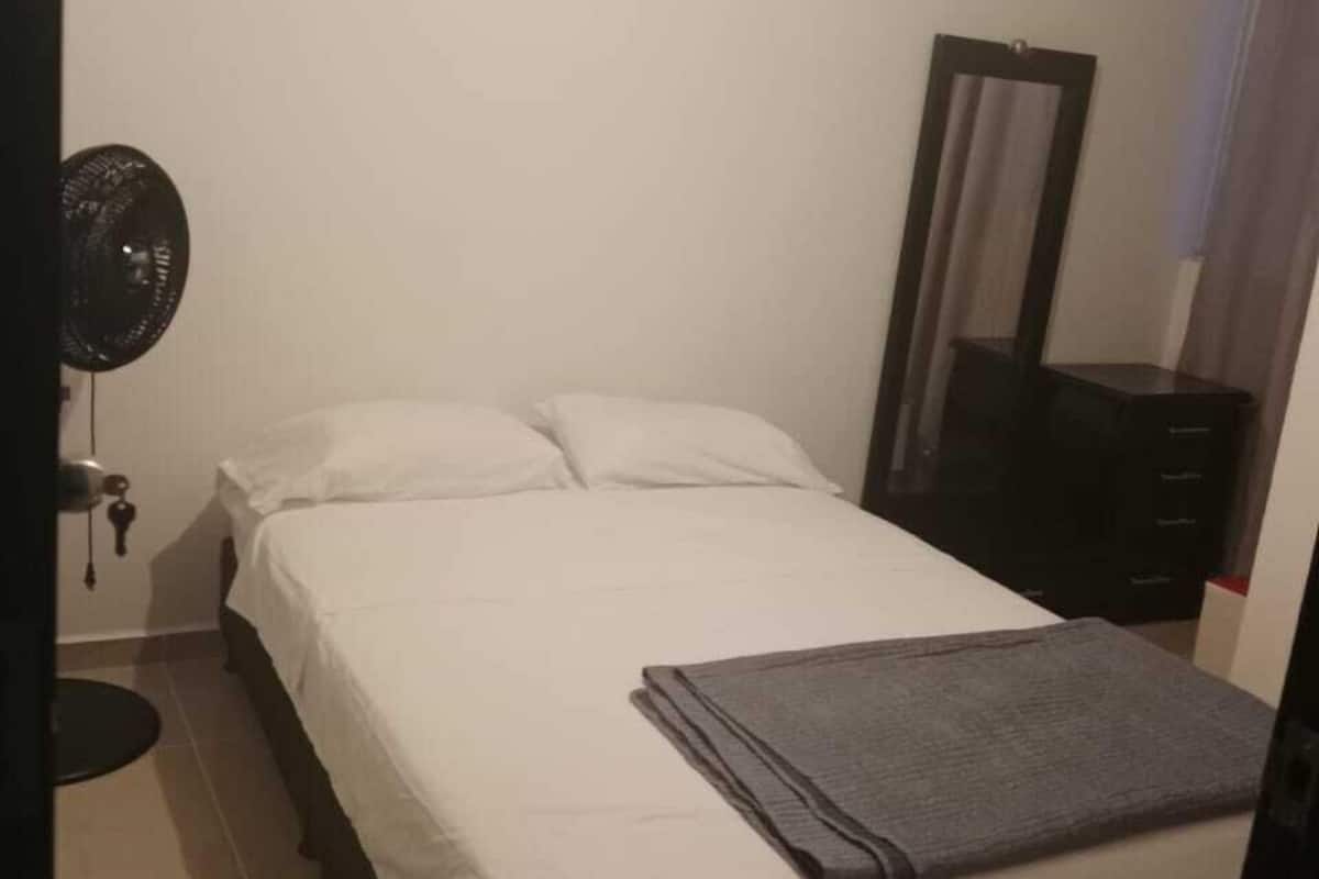 A bedroom with a bed, a bedside table, a mirror, and a fan.