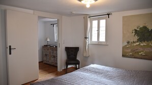 A bedroom with a bed, a chair, a painting, and a window with curtains. - The small guest house in the heart of the historic old town of Dinkelsbühl. (Dinkelsbühl)