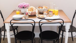 Une table de petit-déjeuner avec une variété d’aliments, notamment des viennoiseries, un saladier de fruits et une carafe de jus d’orange.