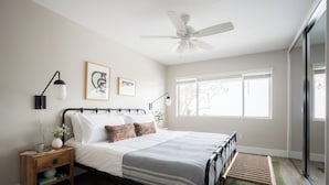 Une chambre à coucher avec un lit, des tables de chevet, un ventilateur de plafond et une fenêtre.