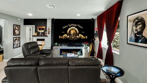 A modern living room with a black leather sofa, a flat-screen TV, and a fireplace. - Desert Hollywood UofA (Tucson)