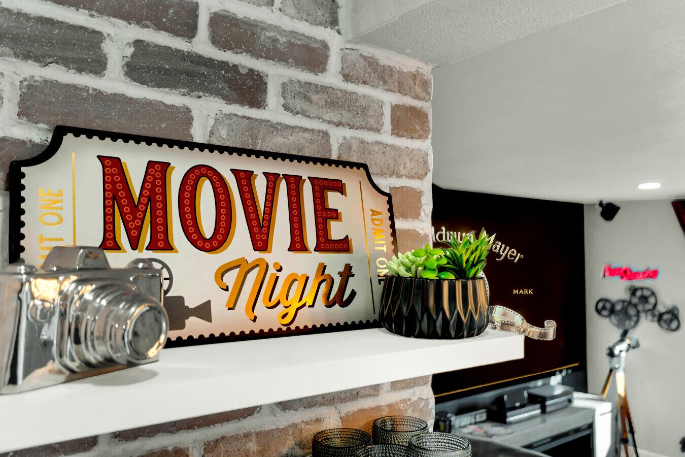 En mur af mursten med et 'MOVIE Night' skilt, et gammelt kamera og en plante på en hylde.