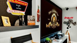 A modern living room with a flat-screen TV, a cinema sign, a framed picture, and a decorative bottle. - Desert Hollywood UofA (Tucson)
