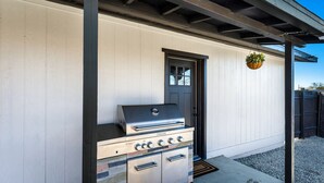 An outdoor kitchen with a grill, a door, and a hanging plant. - Desert Hollywood UofA (Tucson)