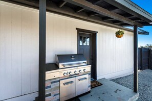 An outdoor kitchen with a grill, a door, and a hanging plant. - Desert Hollywood UofA (Tucson)