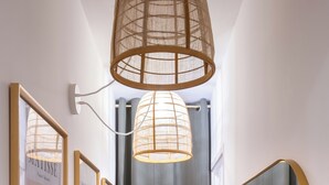 Un couloir orné de tableaux encadrés, un luminaire suspendu, un miroir et un rideau gris.