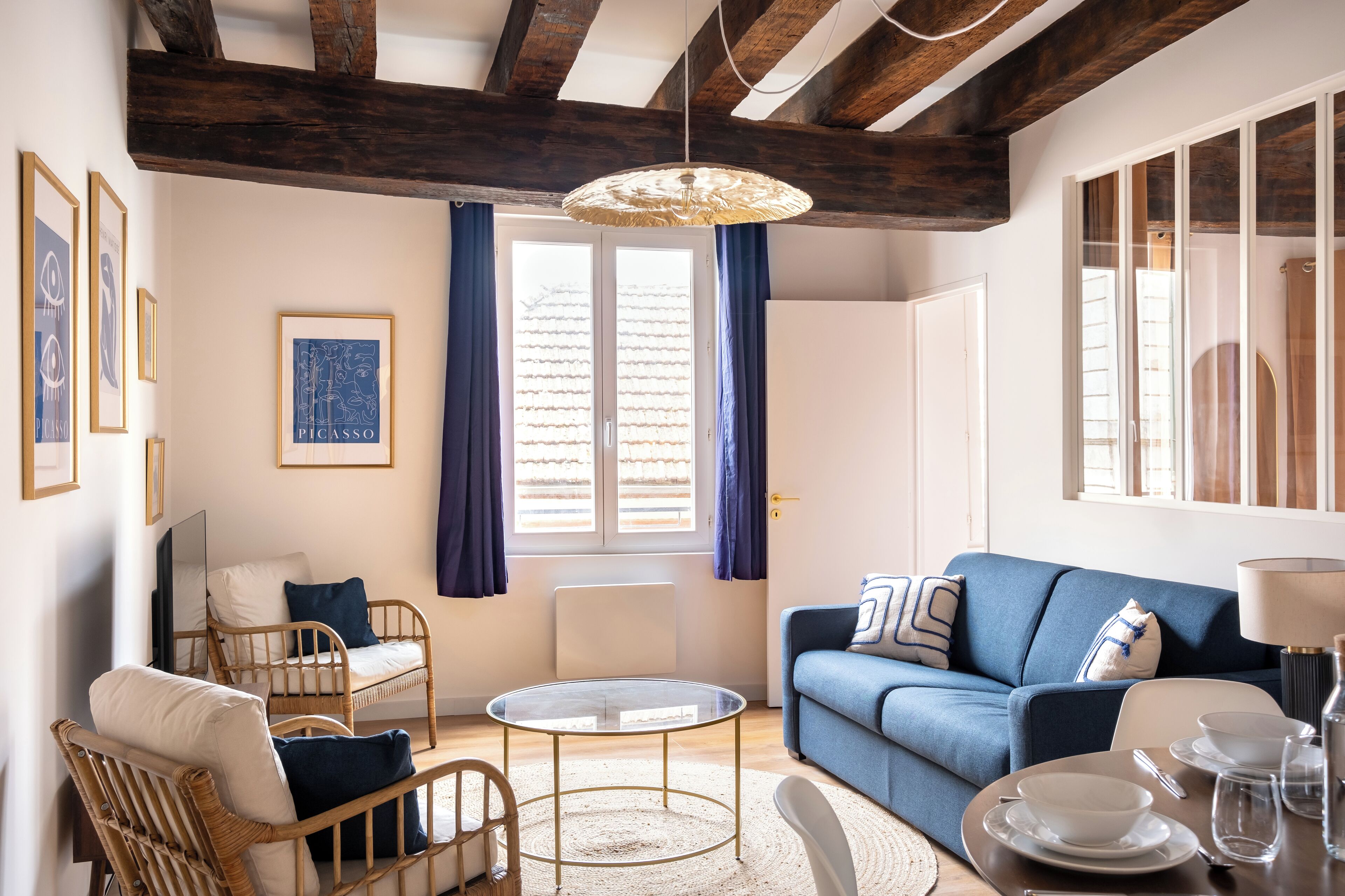 Un salon chaleureux avec un canapé bleu, des fauteuils en osier, une table basse en verre et un ensemble de salle à manger.
