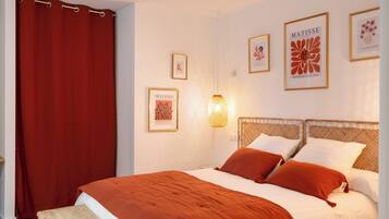 Une chambre à coucher bien aménagée, avec un grand lit, un rideau rouge et des œuvres d’art accrochées au mur, dont une œuvre de Matisse.