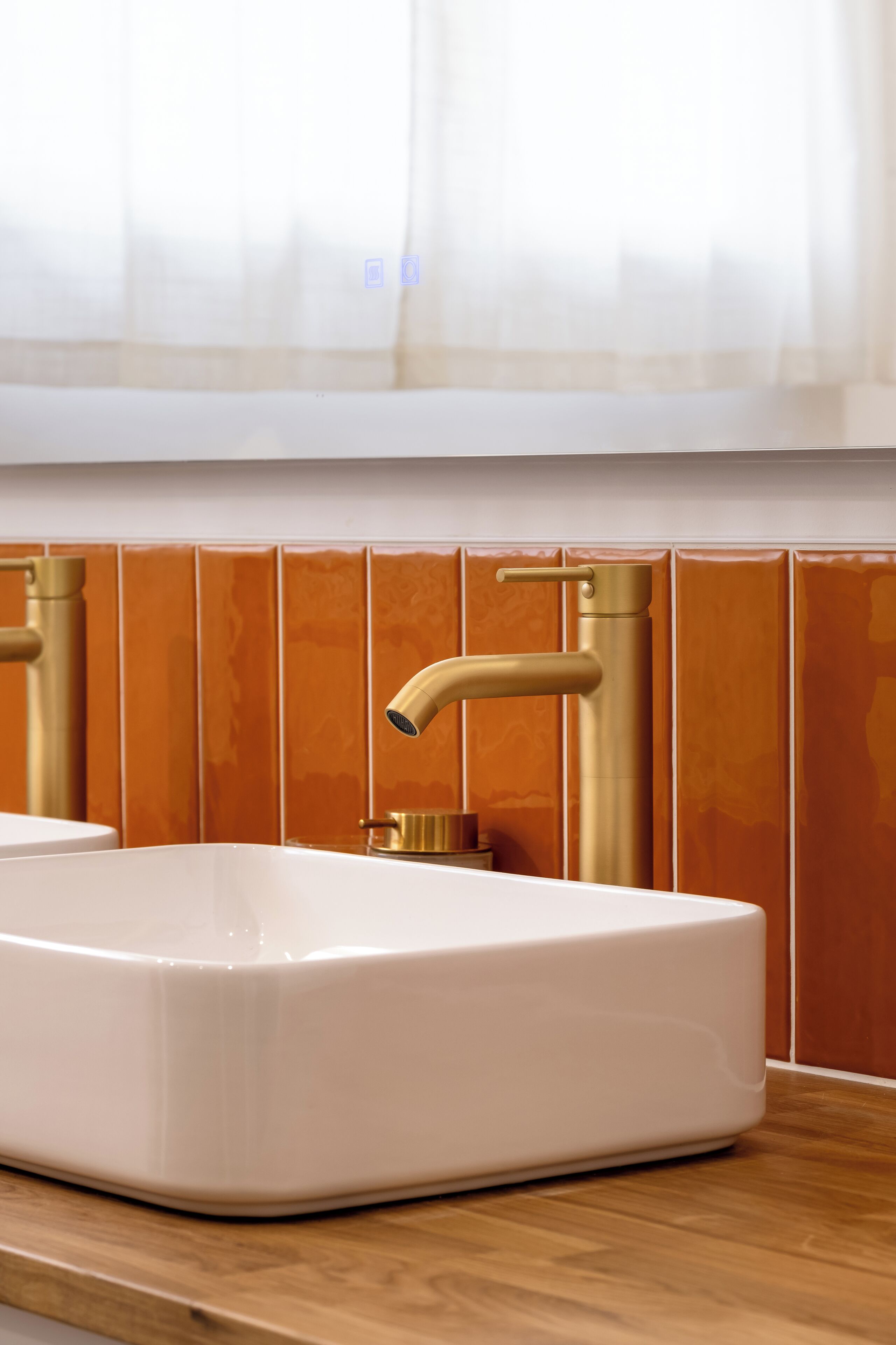 Une salle de bain avec un lavabo blanc, des robinets dorés et des murs recouverts de carreaux orange.