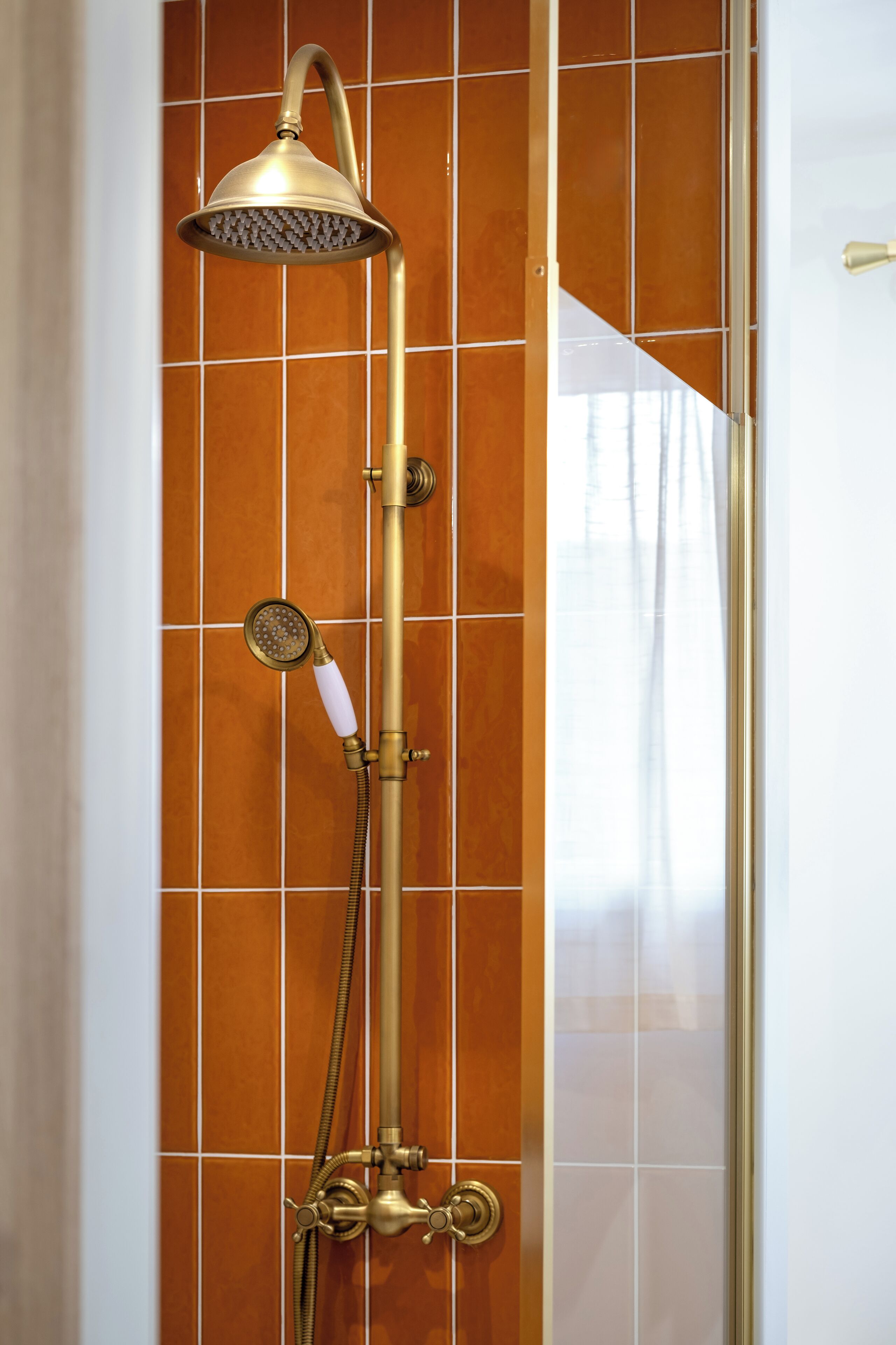 Une douche équipée d’un pommeau de douche à main et d’un pommeau de douche fixé au mur, tous deux dotés d’accessoires dorés, le tout installé devant un mur carrelé.