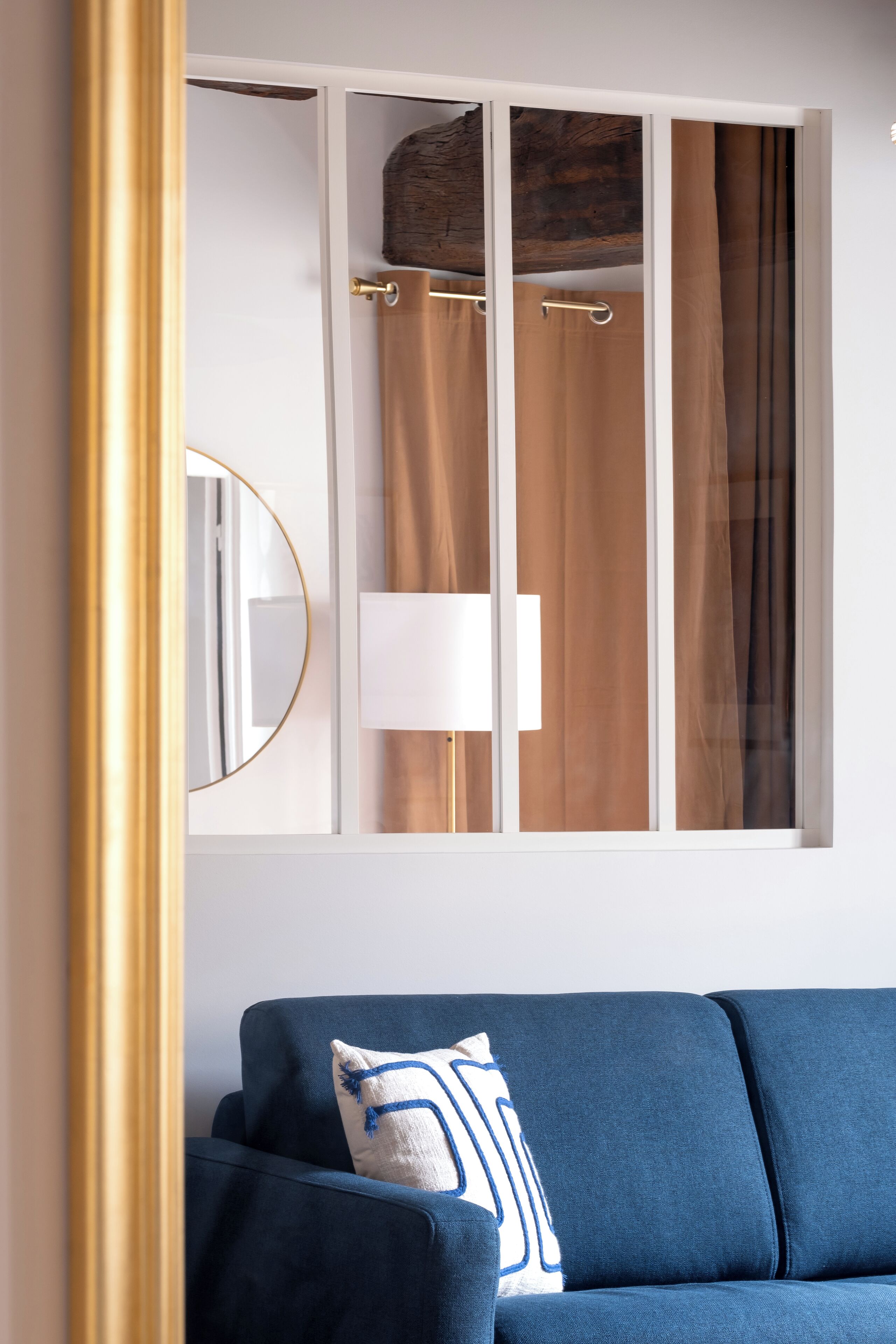 A room with a blue sofa, a large mirror, and a window with curtains.