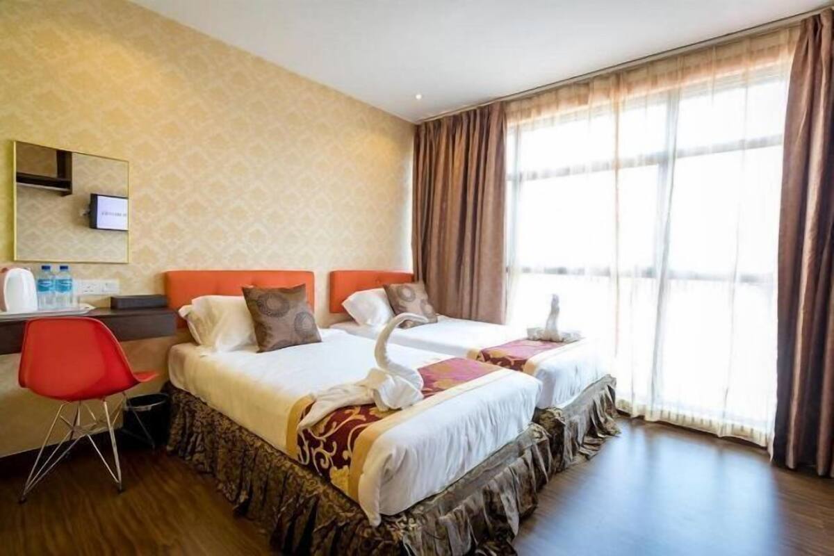 Hotellihuone, jossa on kaksi sänkyä, työpöytä, tuoli, peili ja suuri ikkuna, jossa on verhot.