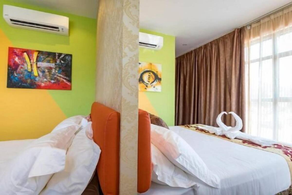 Hotellihuone, jossa on kaksi sänkyä, suuri ikkuna, jossa on verhot, ja taideteoksia seinillä.