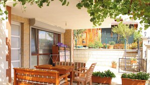 An outdoor patio with a wooden table and chairs, potted plants, and a view of a building in the background. - Şahan Apart (Yesilova)