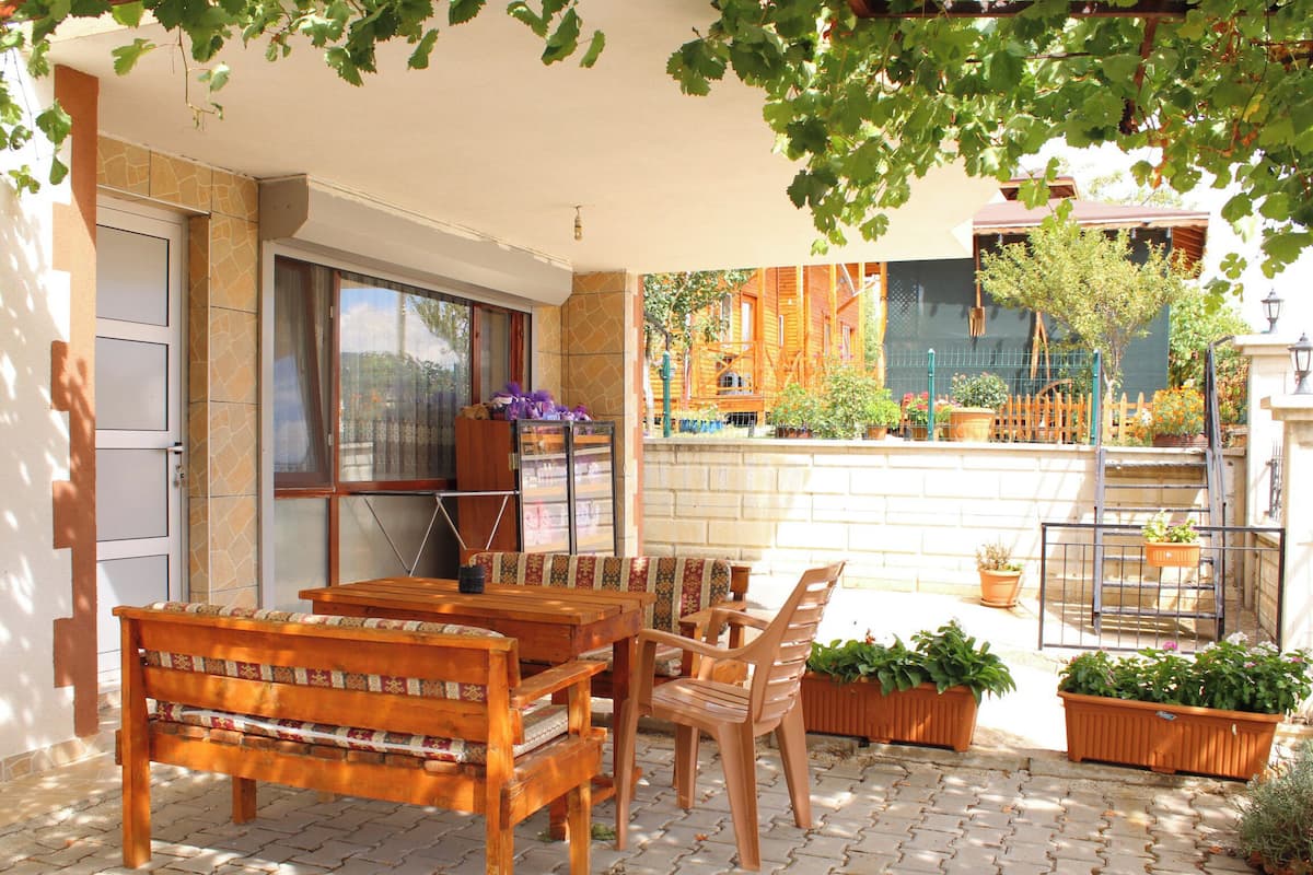 Un patio al aire libre con una mesa y sillas de madera, plantas en macetas y una vista de un edificio al fondo.