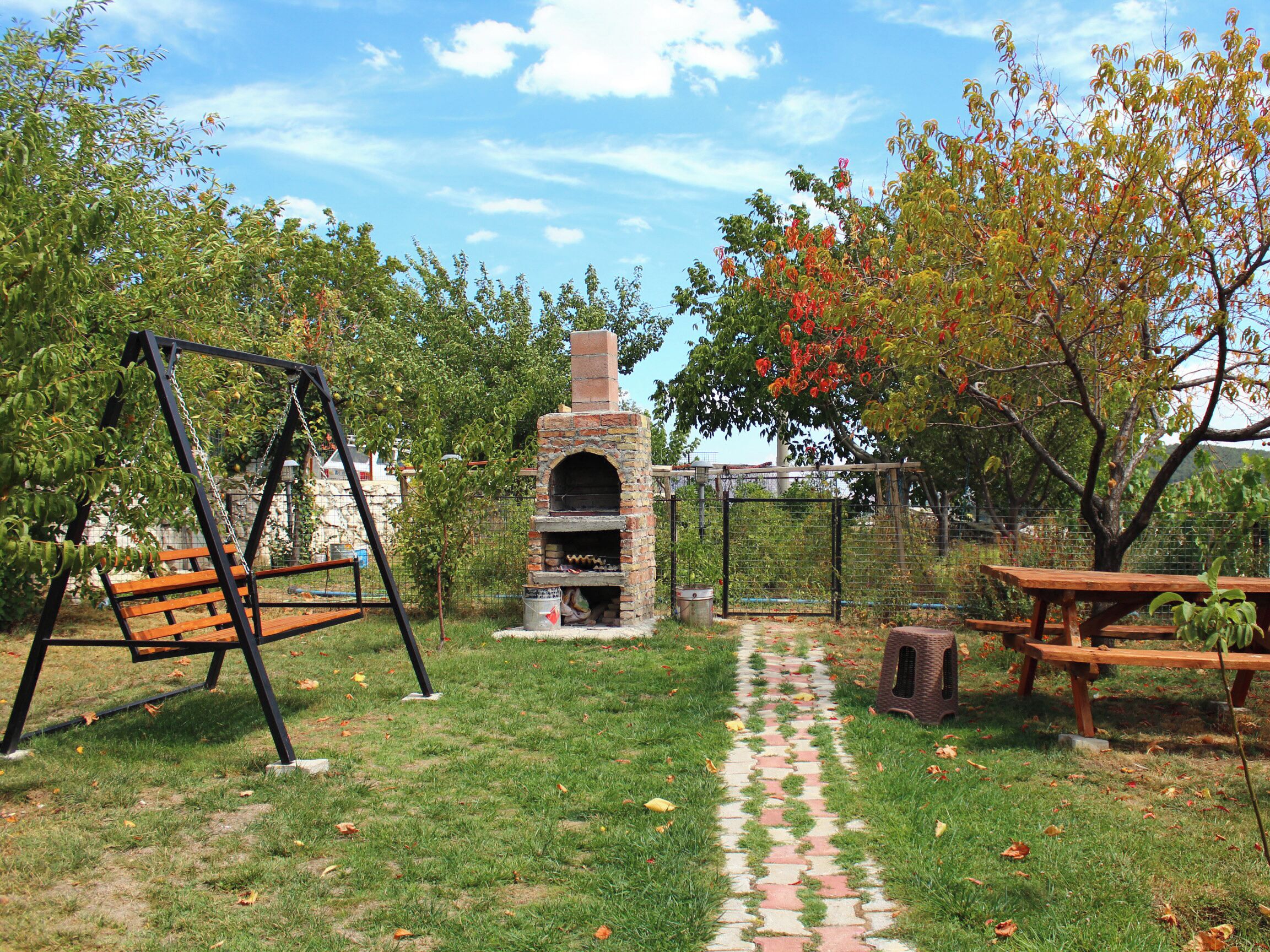 Un giardino sul retro con un forno in mattoni, altalene e tavoli da picnic.