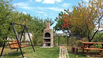 Un giardino sul retro con un forno in mattoni, altalene e tavoli da picnic.