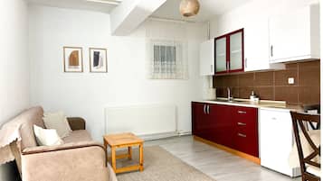 Um espaço compacto para viver com sofá, uma pequena mesa de madeira, área de cozinha com armários vermelhos e um radiador.