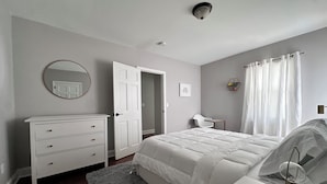 Ein Schlafzimmer mit Bett, Kommode, Spiegel und einer Tür zu einem anderen Raum.