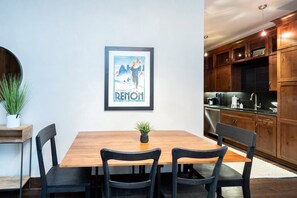 Un comedor con mesa y sillas de madera, un cuadro en la pared y armarios de madera al fondo.