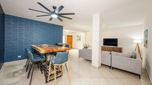 Un salon moderne comprenant un coin repas, un canapé gris, un téléviseur et un ventilateur de plafond.