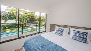 Une chambre dotée d’une grande fenêtre donnant sur une piscine et une végétation luxuriante.