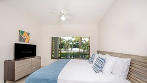 Une chambre à coucher avec un lit, un téléviseur posé sur une commode, un ventilateur de plafond et une vue sur la verdure à l’extérieur.