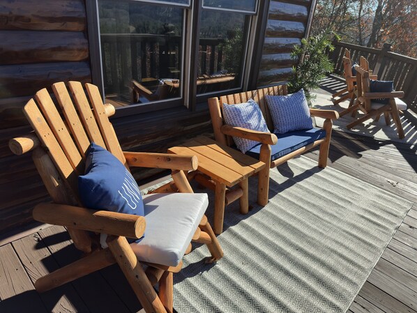 A wooden deck with Adirondack chairs and a patterned rug.