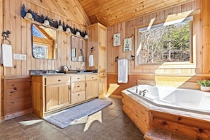 Relax in a spacious bathroom with a large vanity, sink, and bathtub, surrounded by natural light and forest views.