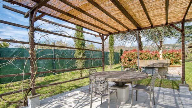 Un patio exterior con un pérgola, una mesa y dos sillas.