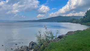 Un lago tranquilo con orilla cubierta de hierba y una cadena montañosa distante bajo un cielo parcialmente nublado.