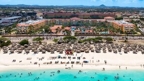 Resort com uma extensa área de praia, várias piscinas e um edifício de hotel imponente com telhado vermelho.