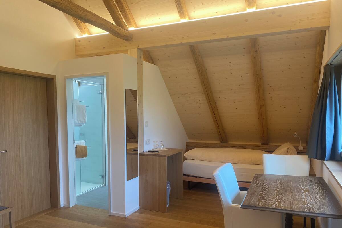 Una habitación pequeña y acogedora con techo inclinado, una cama, un escritorio y una silla.