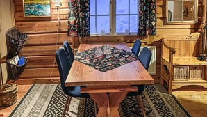 Une table à manger en bois, agrémentée d’un chemin de table à motifs floraux, entourée de chaises bleues, dans une pièce au style rustique, avec une fenêtre et un miroir.