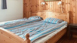 Un lit en bois avec une literie à rayures, dans une pièce aux murs en bois et dotée d’une table de chevet.