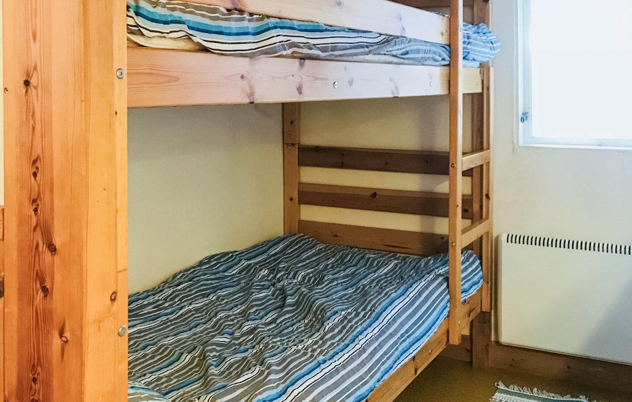 A bunk bed with striped bedding, a window with blinds, and a radiator.