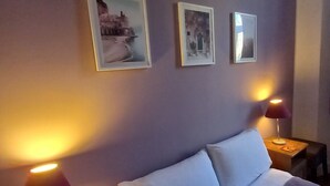 A hotel room with a bed, two bedside lamps, and three framed pictures on the wall.