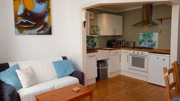 A compact living space with a kitchenette, a sofa with cushions, and a wooden coffee table.