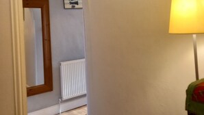 A hallway with a white radiator, a framed painting of a ship on the sea, and a lamp with a green lampshade.