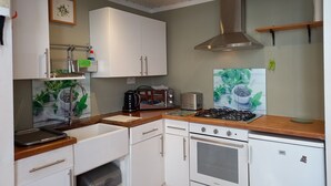 A compact kitchen with white cabinets, a gas stove, a built-in oven, and a coffee maker.