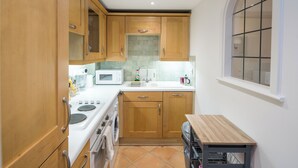 A compact kitchen with wooden cabinets, a microwave, a sink, and a window with a grid pattern. - 1BD Modern City Oasis: Near London Attractions (London)