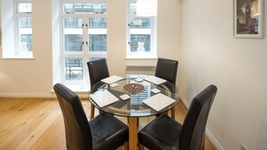 A round glass table with six chairs, large windows with blinds, and a framed picture on the wall. - 1BD Modern City Oasis: Near London Attractions (London)