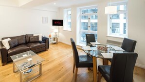 A modern living room with a brown leather sofa, a glass coffee table, and a dining area with a glass table and black chairs. - 1BD Modern City Oasis: Near London Attractions (London)