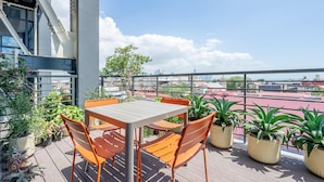 Terraza en la azotea con una mesa y sillas, rodeada de plantas en macetas, con vistas a un paisaje urbano.
