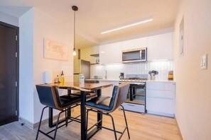 Une cuisine moderne avec des meubles blancs, un four à micro-ondes et un coin repas comprenant deux chaises et une table.