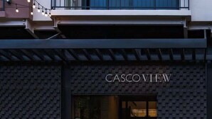 L’entrée d’un immeuble est surmontée d’une enseigne portant le nom « CASCOVIEW », un escalier mène à l’entrée et des plantes en pot sont disposées sur le trottoir.