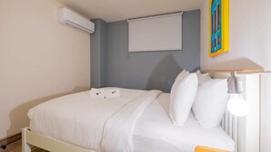 Een slaapkamer met een bed, witte beddengoed, een airconditioning, een raam met een blind en een wandlamp.