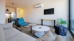 Een moderne woonkamer met een bank, een blauwe stoel, een ronde salontafel en een bijzettafeltje.